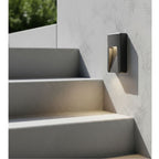 Brecon Oblong LED Wall & Step Light in graphite mounted on a rendered wall beside outdoor steps