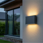 Brecon Slim LED Up & Down Wall Light in graphite mounted on an exterior wall beside a garden