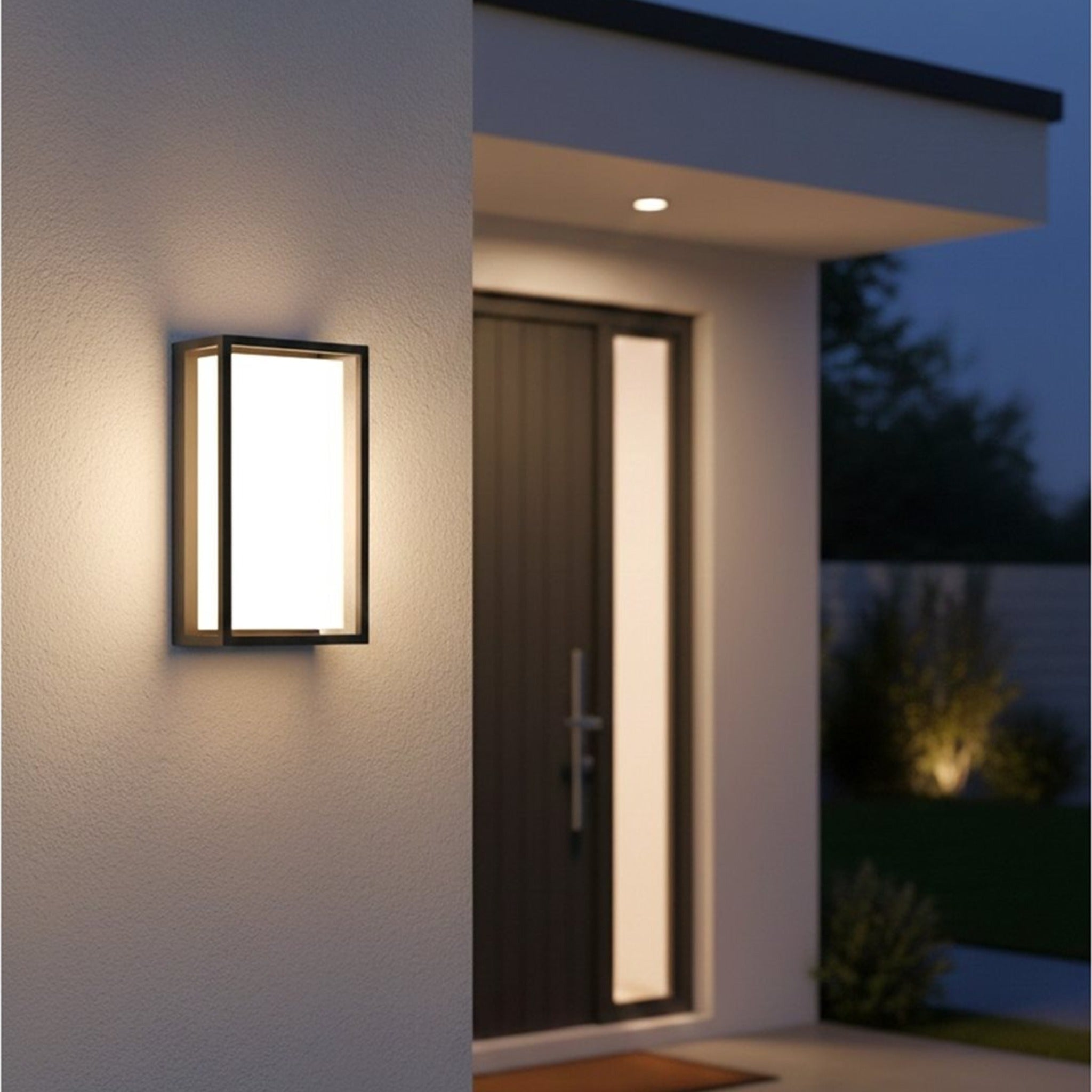 Elgin Framed Panel LED Outdoor Wall Light in graphite lit at night, casting warm light down a wall