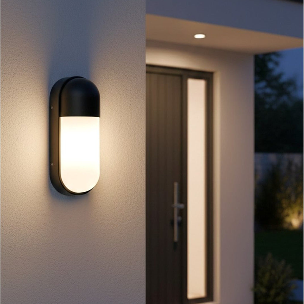 Elgin Oval Bulkhead Outdoor Wall Light in black, mounted beside a front door at dusk