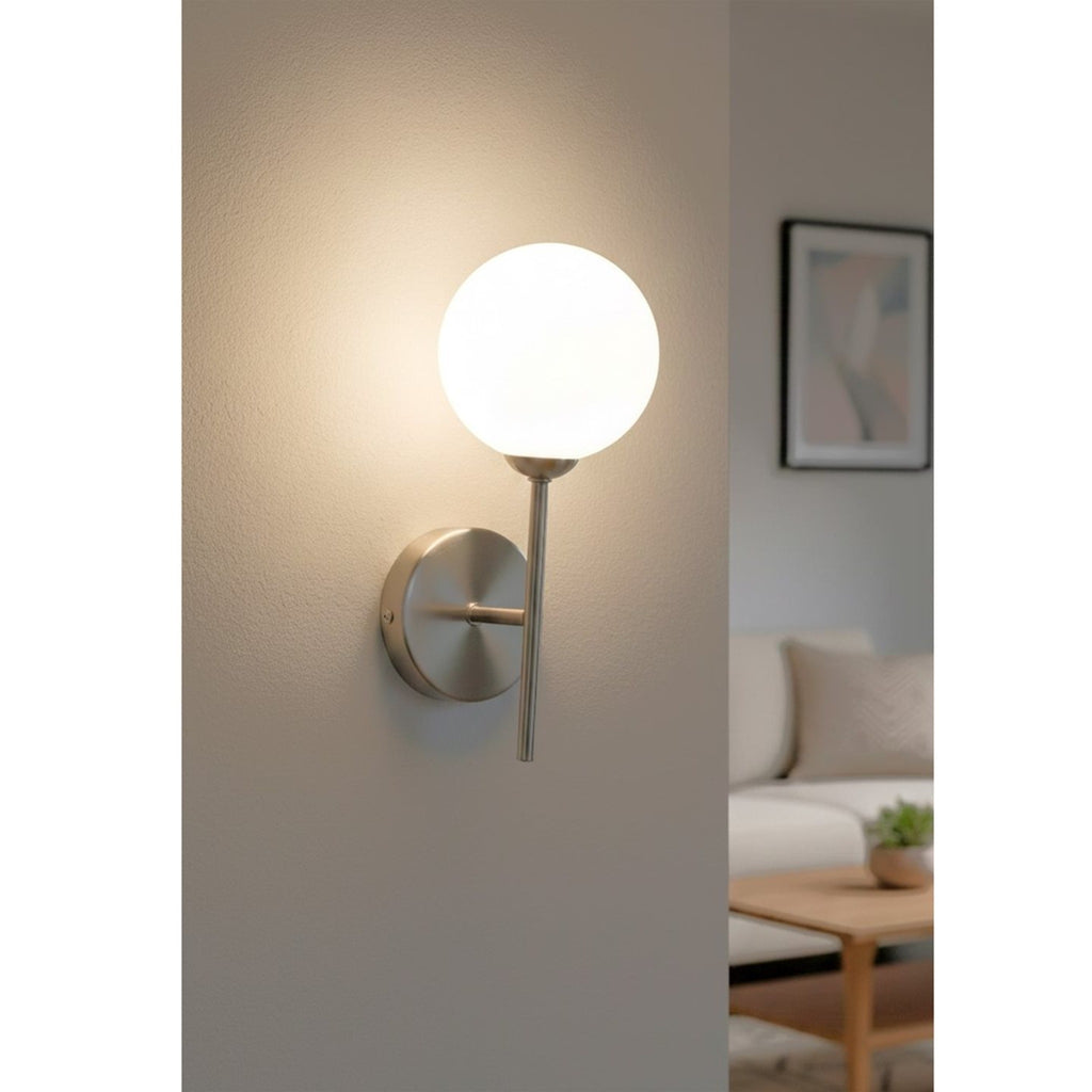 Ellis Globe Wall Light in brushed steel lit on a living room wall