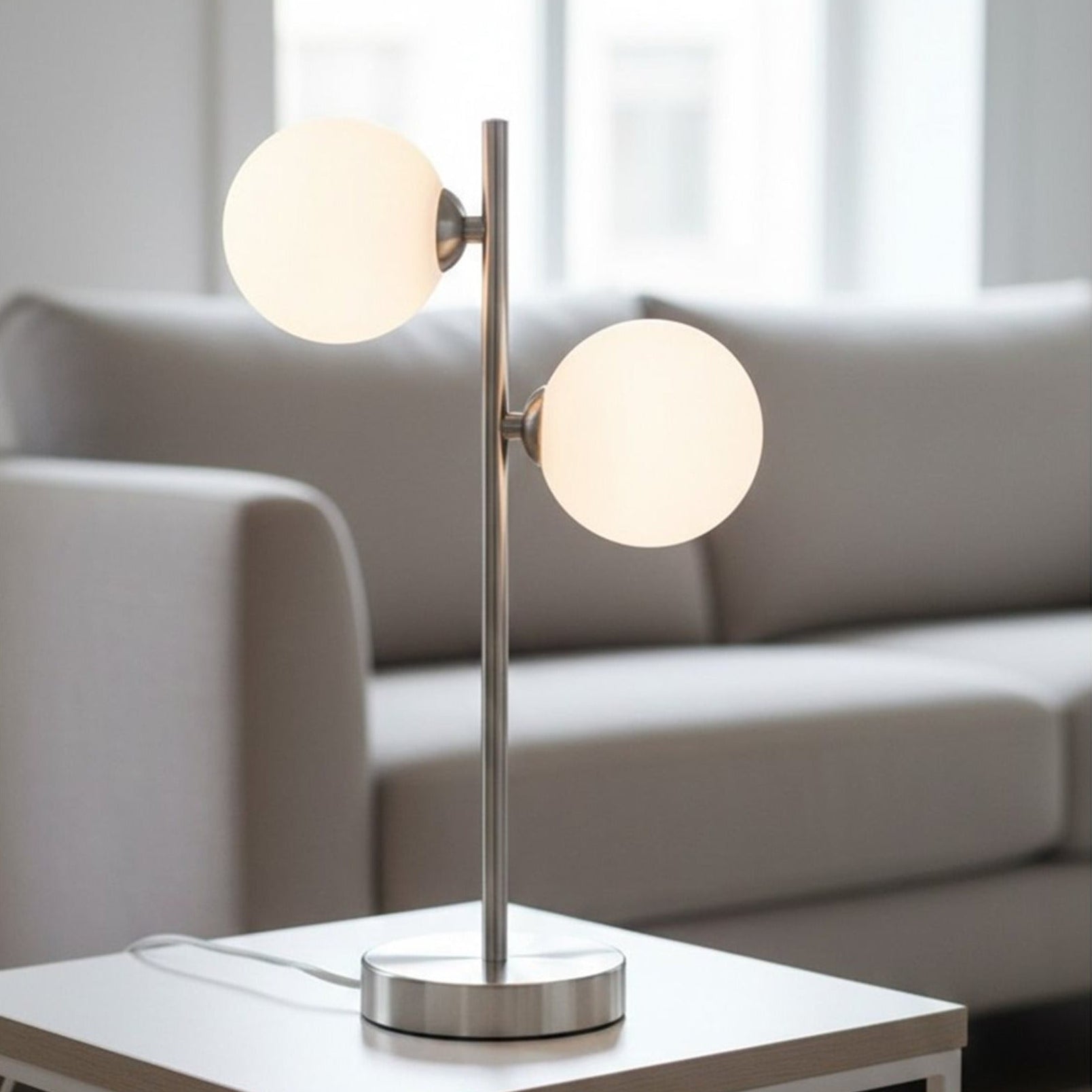 Ellis Twin Globe Table Lamp in brushed steel on a living room side table beside a sofa