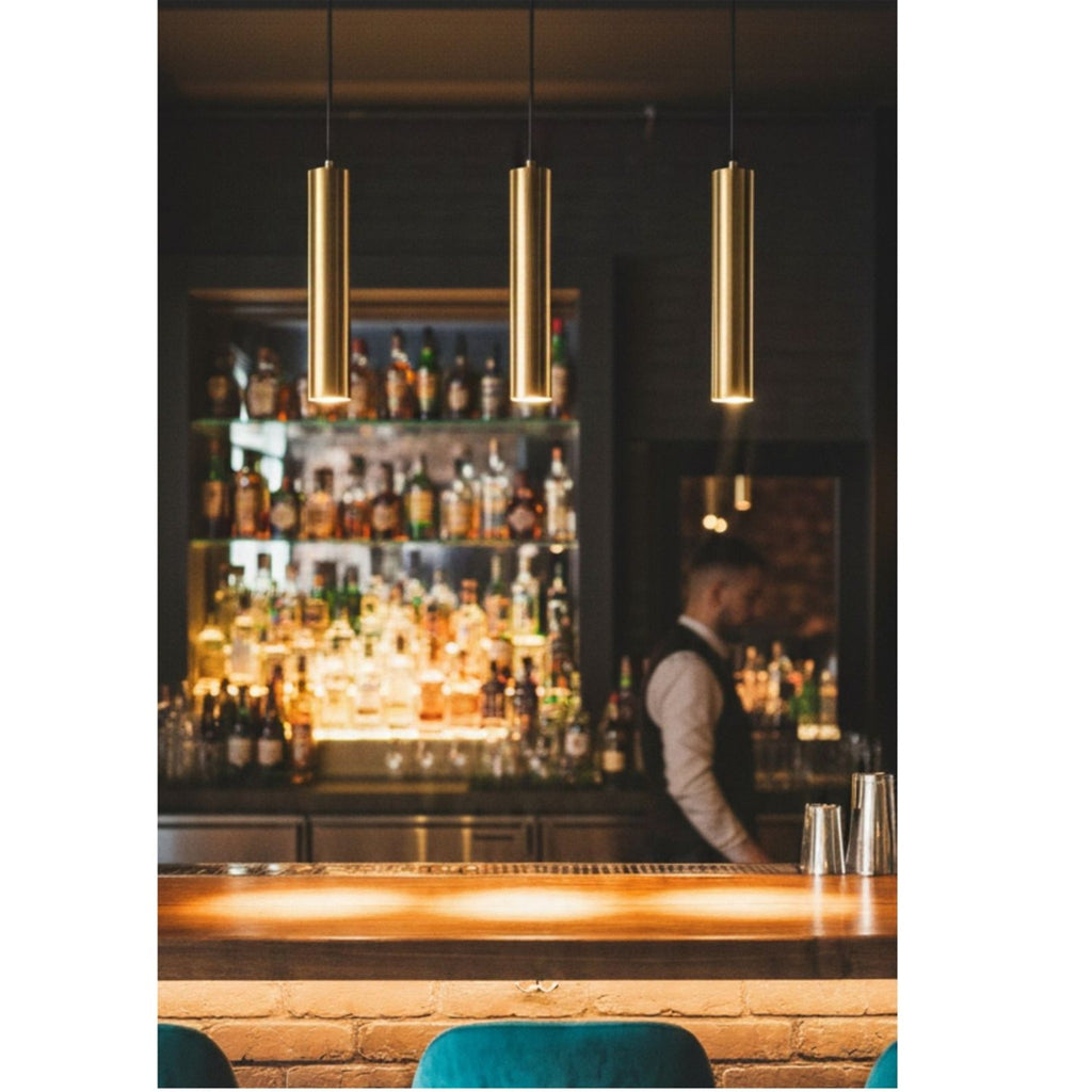 Three satin brass Kelso pendants hanging in a row above a bar counter