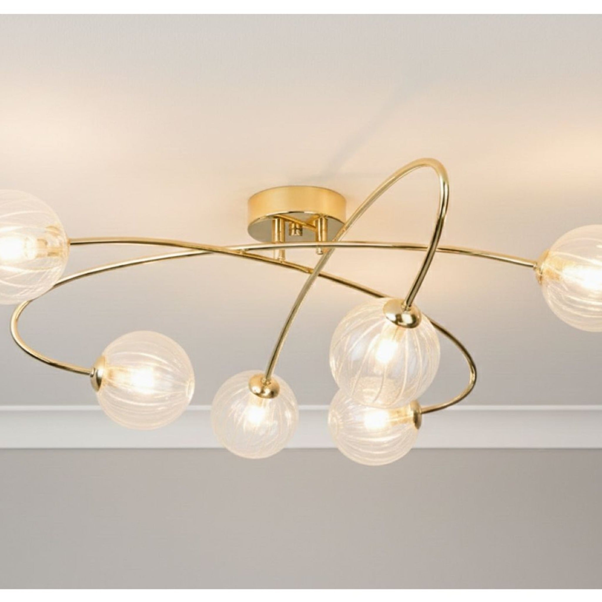 Linden Swirled Glass 6 Light Flush Ceiling Light in brass, lit on a ceiling