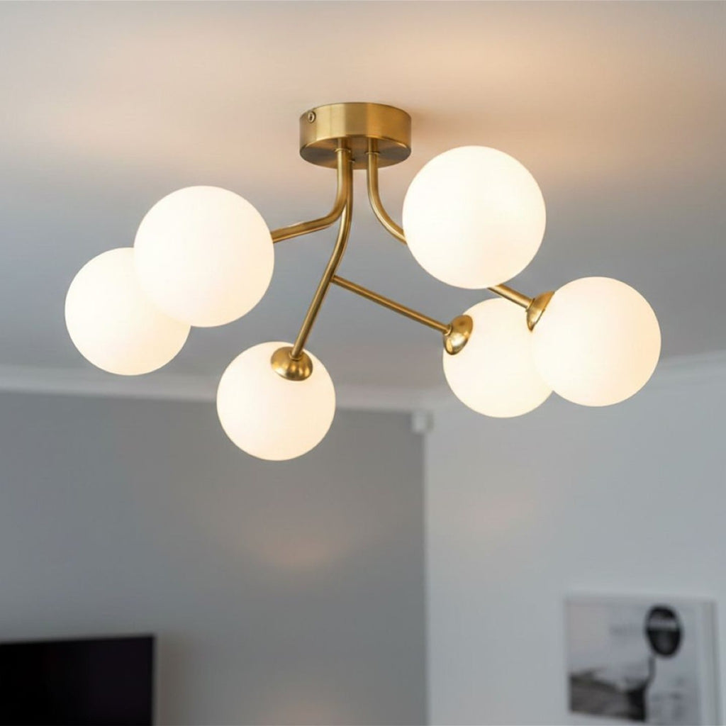 Lyra 6 Globe Flush Ceiling Light in brushed brass lit on a living room ceiling