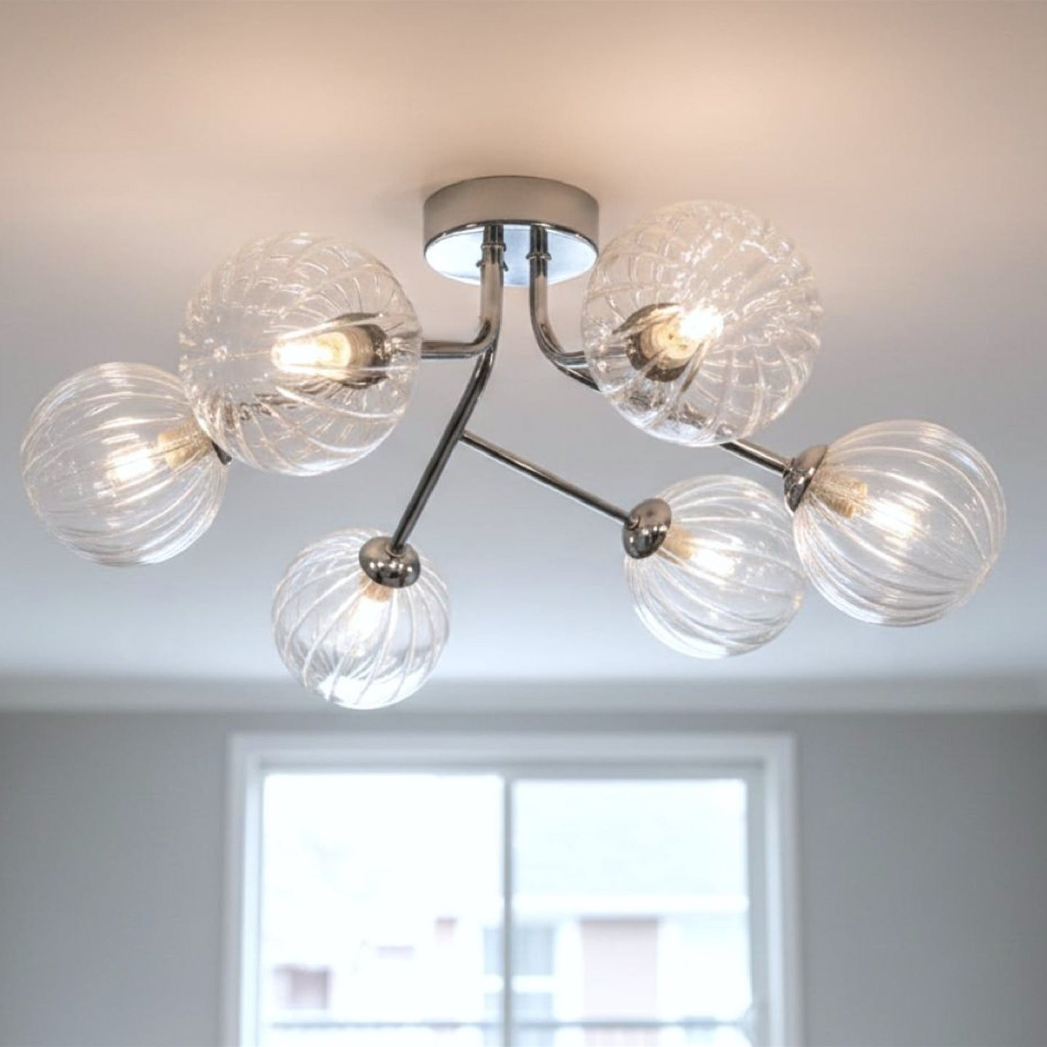 Lyra 6 Globe Flush Ceiling Light in chrome lit on a ceiling above a bright window