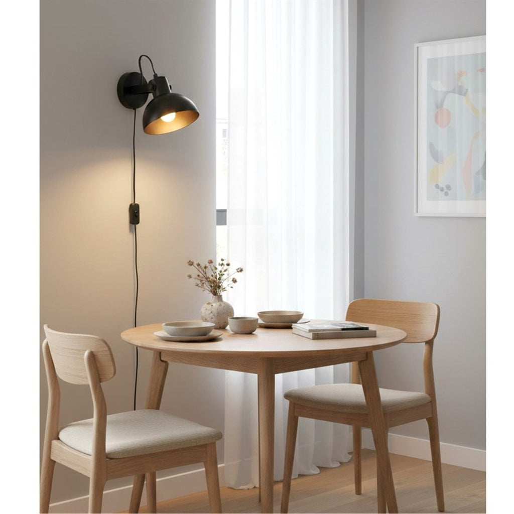 Nyla Plug-In Dome Wall Light in black, lit above a dining table in a bright room