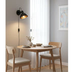 Nyla Plug-In Dome Wall Light in black, lit above a dining table in a bright room