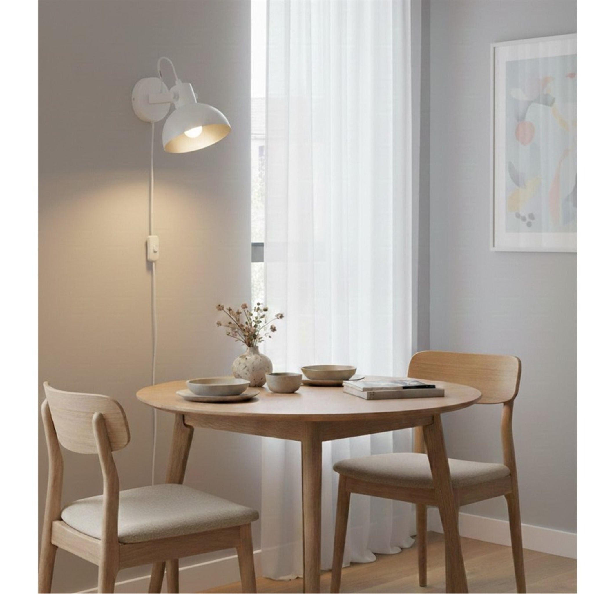 Nyla Plug-In Dome Wall Light in white, lit above a dining table in a bright room