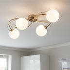 Orla Swirl Globe 4 Light Flush Ceiling Light in brushed brass lit on a room ceiling