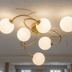 Orla Swirl Globe 6 Light Flush Ceiling Light in brushed brass lit on a room ceiling
