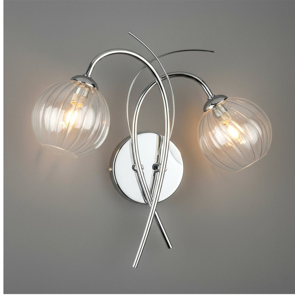 Orla Swirl Globe Wall Light in chrome lit against a grey wall
