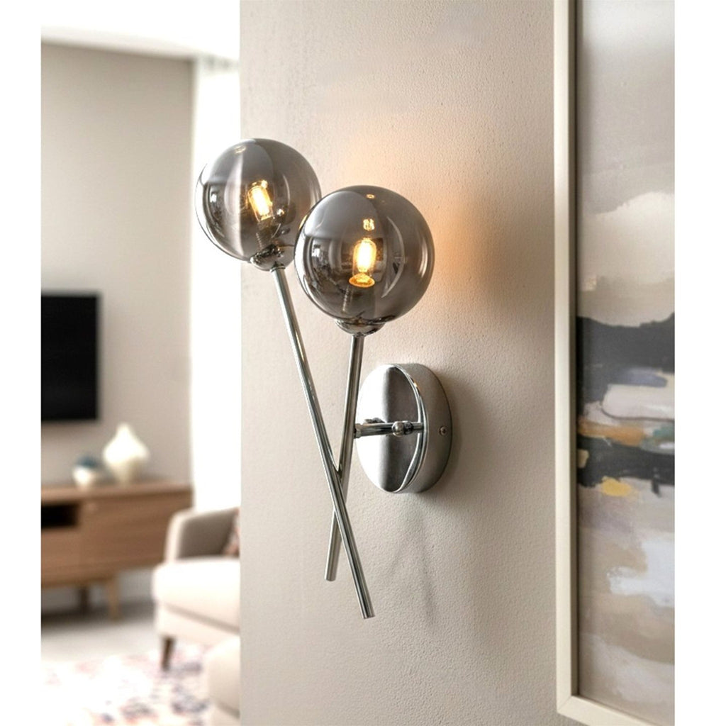 Ripley Glass Globe 2 Light Wall Light in chrome, lit on a living room wall