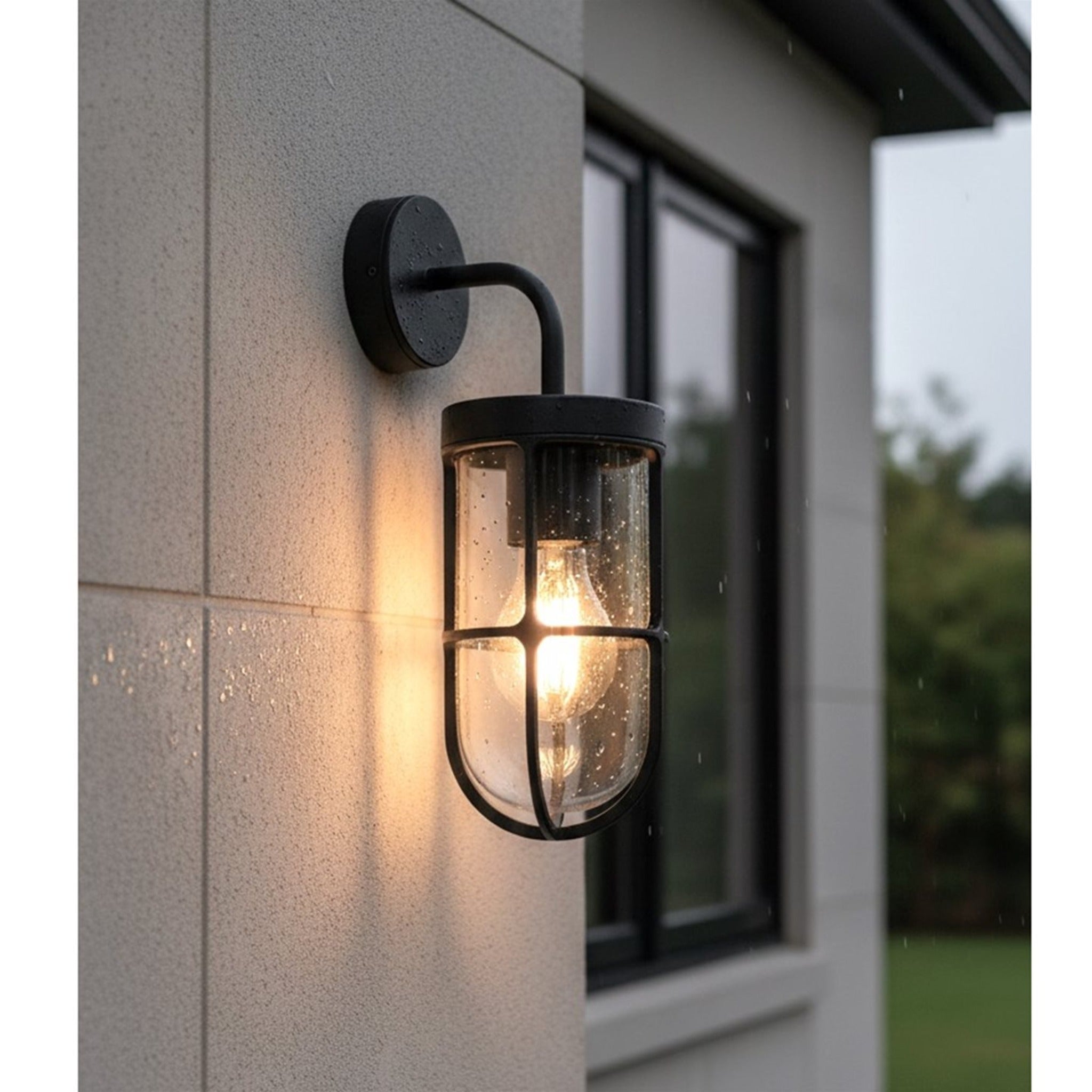 Tarbet Caged Glass Outdoor Wall Light in black, lit on a rendered exterior wall beside a window