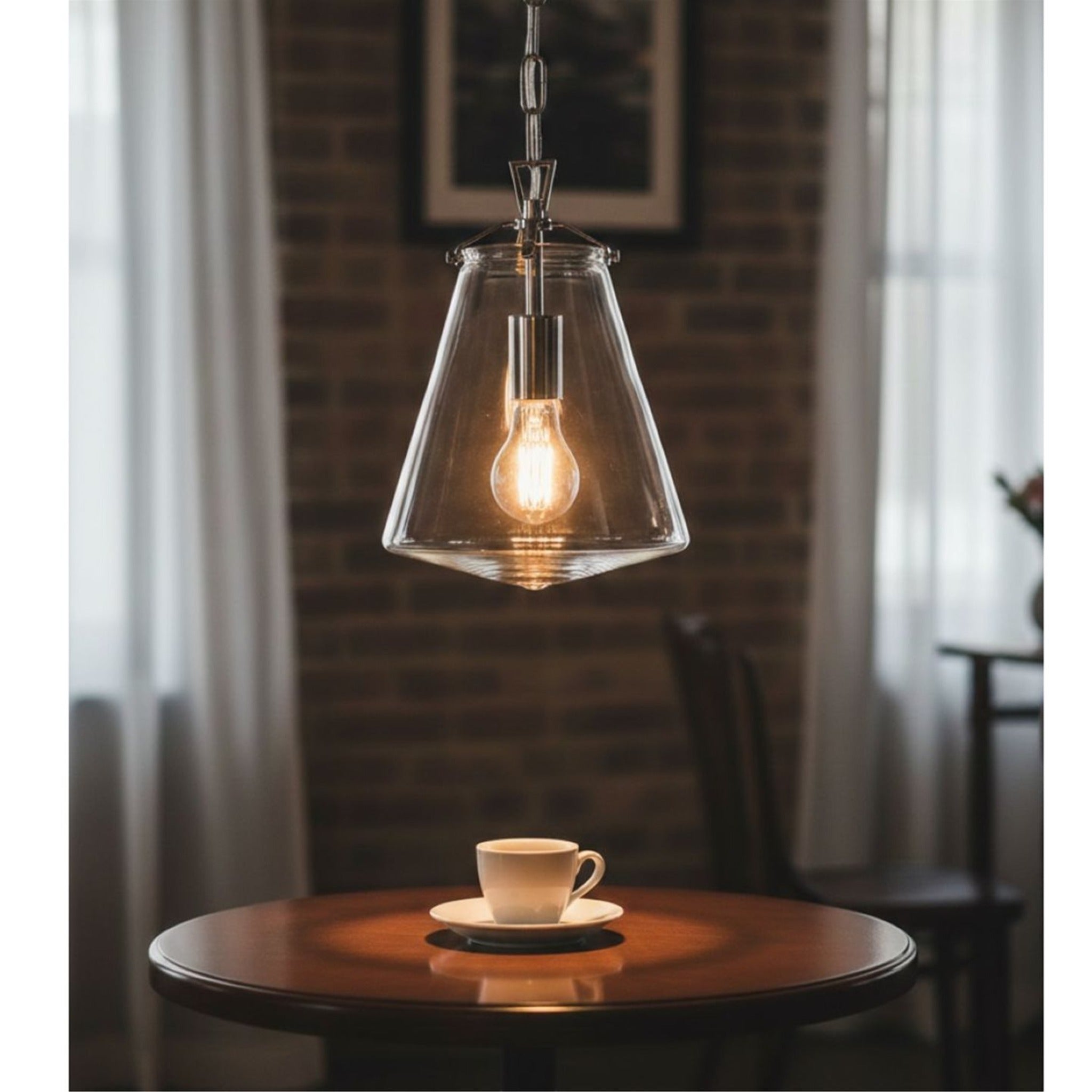 Vela Tapered Clear Glass Pendant in chrome, lit above a cafe table against a brick wall