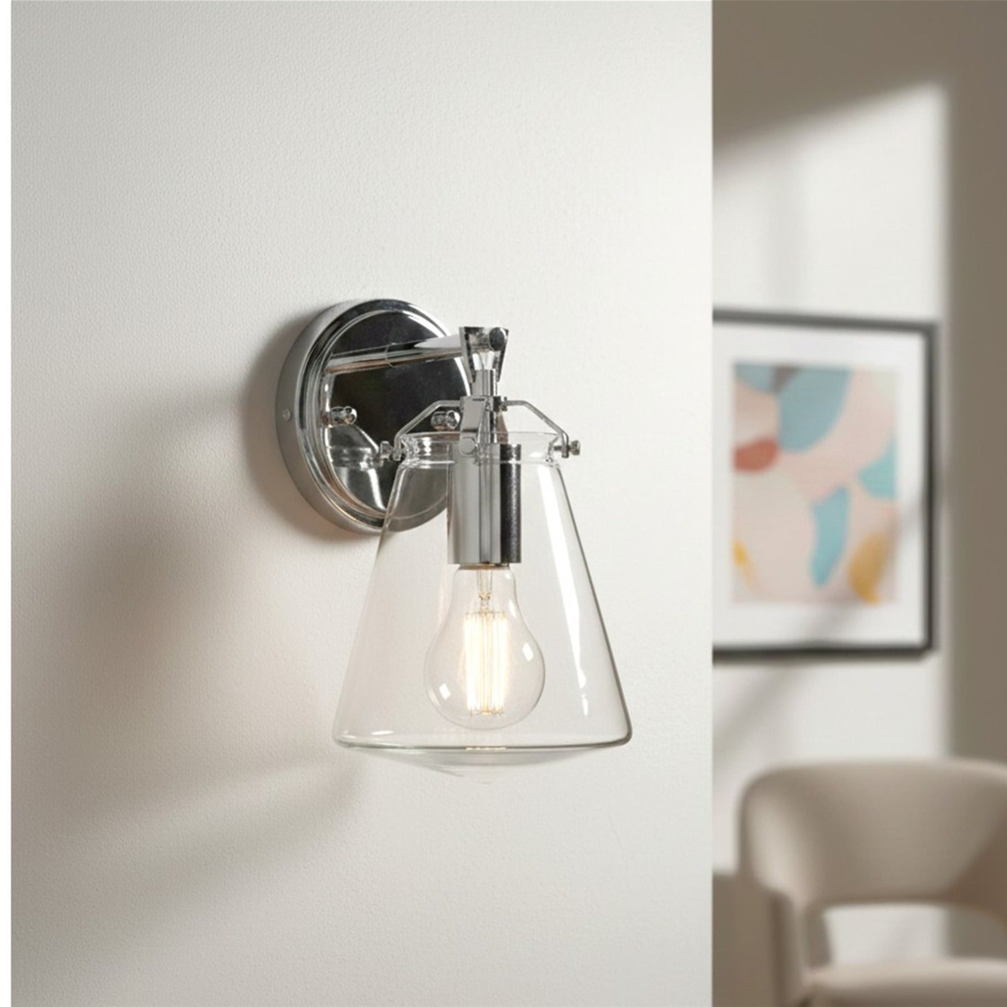 Vela Tapered Clear Glass Wall Light in chrome, mounted on a living room wall